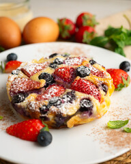 Delicious sweet clafoutis tart with blueberries and strawberries baked using a traditional French recipe.