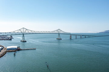 Aerial drone view of the Astoria-Megler Bridge stretching across the Columbia River, connecting Oregon and Washington, with calm blue waters and a clear sky
