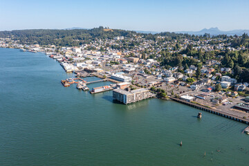 Obraz premium Aerial drone view of downtown Astoria, Oregon, featuring waterfront buildings, the Columbia River, a busy port, fishing boats, and lush hills in the background