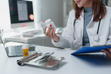 Fototapeta premium Female doctor is holding a pill bottle and reading a patient's medical chart while sitting at her desk in a modern clinic office, demonstrating her expertise in healthcare and medicine