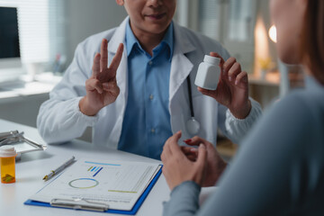Doctor showing medicine bottle and explaining dosage to patient during consultation in medical...