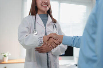 Smiling female doctor shaking hands with a patient in a bright medical office, conveying empathy...