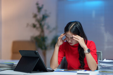 Young businesswoman feeling overwhelmed and fatigued while working late at night in the office,...