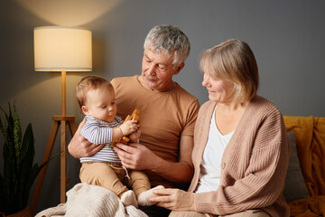 Two grandparents enjoy quality time with their grandchild in a comfortable living room. The child...