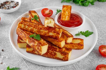 Fried halloumi cheese sticks with tomato sauce on a white plate on a concrete background.