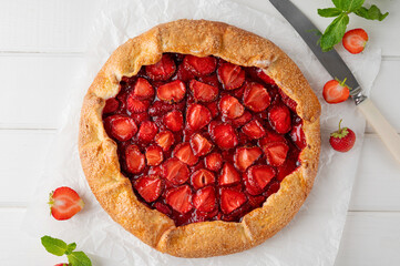 Galette, open pie or tart with strawberries with cup of tea on a white wooden table. Summer sweet pie.