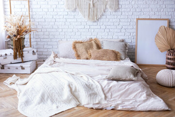 Cozy bedroom with interior design in boho style, bed mattress on floor, cushions, frame poster, home decor, stepladder, macrame panel against white brick wall. Concept of classy house and apartment.   © stock_studio