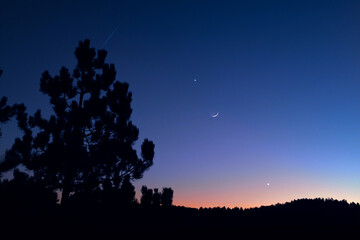 Countryside silhouettes under the stars, meteor trail and crescent Moon.