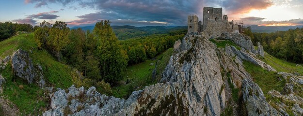 Panorama Old castle ruins on a rocky cliff, the famous fortress in ruin. Panoramic view of nice castle during scenic sunrise lighting sky with clouds and landscape. © Ivan