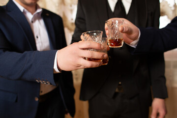 Three people in suits hold glasses with an amber-colored drink in their hands.