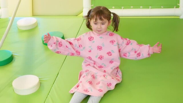 A 5-year-old mixed Korean-Ukrainian girl slides down a bright green play area in slow motion, wearing a pink floral dress with pigtails joyfully, arms wide open