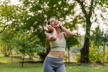 Young Asian Woman Enjoying Music while Stretching Outdoors. Beautiful Fit Lady Practicing Fitness...
