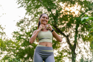 Young Asian Woman Enjoying Music while Stretching Outdoors. Beautiful Fit Lady Practicing Fitness...