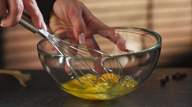 Woman beating eggs in a glass bowl with a hand mixer. Slow motion