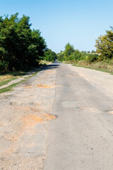 Bad road, cracked asphalt with potholes and big holes. The asphalt surface is destroyed on the road.
