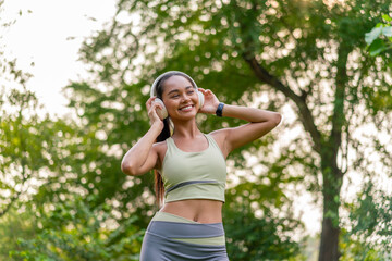 Young Asian Woman Enjoying Music while Stretching Outdoors. Beautiful Fit Lady Practicing Fitness...