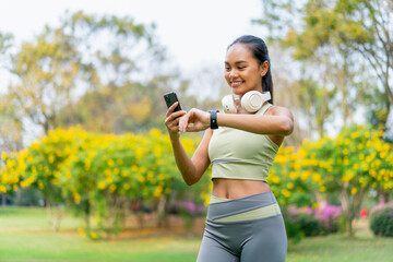 Asian Woman Using Smartwatch and Phone During Outdoor Workout. Fitness and Technology Integration...