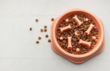 Dry pet food is in a slow feeder bowl on a tiled floor