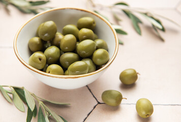 Green olives spilling from bowl onto tiled surface with olive branches