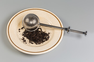 Fototapeta premium Stainless steel tea strainer on saucer with black tea leaves