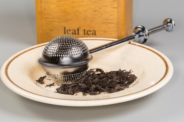 Stainless steel tea strainer on saucer with black tea leaves
