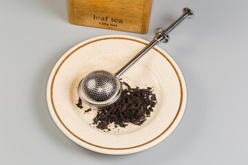 Stainless steel tea strainer on saucer with black tea leaves