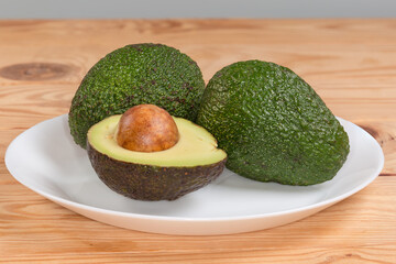 Whole and halved avocado on dish on rustic table