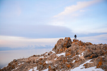 A man stands on the top of a cliff. A traveler stands on the top of a mountain and looks at the sea. Beautiful documentary landscape. Beautiful nature with a rocky mountain and a lake
