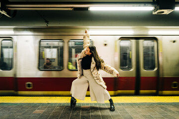 Woman in fur coat strikes dramatic pose on subway platform with train