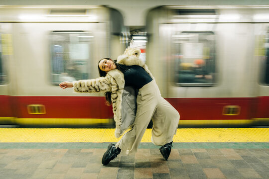 Woman in fur coat dances gracefully on subway platform with train