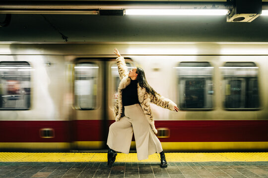 Woman in fur coat poses elegantly on subway platform with moving train