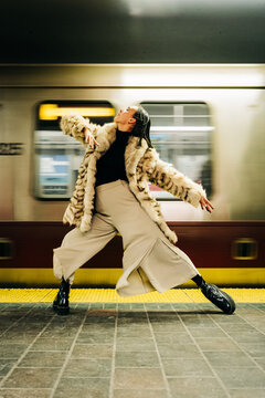 Woman in fur coat poses elegantly on subway platform with moving train