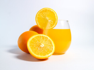 Fresh orange juice in a glass with whole and sliced oranges on a white background