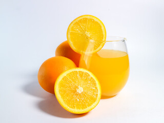 Fresh orange juice in a glass with whole and sliced oranges on a white background