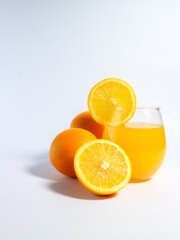 Fresh orange juice in a glass with whole and sliced oranges on a white background