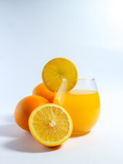 Fresh orange juice in a glass with whole and sliced oranges on a white background