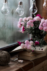 pink flowers in a glass vase on a wooden windowsill against a background of raindrops, books and flowers, garland