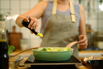 Woman preparing a healthy meal in a kitchen, adding soy sauce into a pan