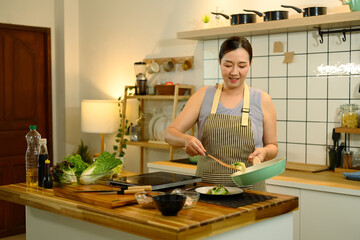Smiling 40s asian woman wearing apron preparing a healthy meal in a modern kitchen