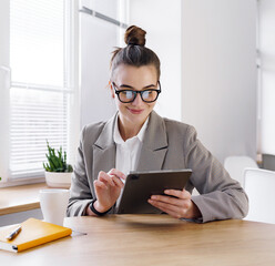 Young woman working on a tablet while sitting at a modern desk in a well-lit office space