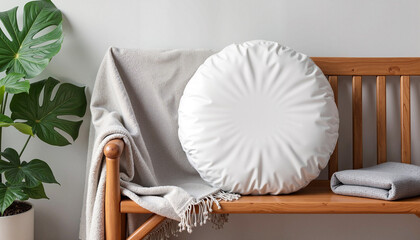 A round pillow mockup styled on a wooden chair, accompanied by a gray throw blanket and a green plant. The natural and inviting aesthetic makes it ideal for presenting home decor designs