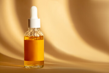 Glass bottle with white dropper lid with orange serum on brown background in sunlight. Essence with vitamin C in transparent unmarked container. Mockup of cosmetic product for skin care