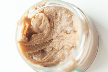 Nut butter in a jar. Homemade nut spread in a clear glass jar on a white background. Freshly ground organic food preparation.