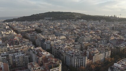 A bird's-eye view of the residential areas, roads and sights of Barcelona on the seashore at the foot of the hill. Drone video in the rays of the rising sun