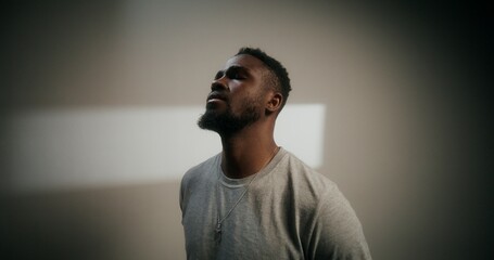 A frustrated man covers his face with trembling hands, standing near a white wall indoors
