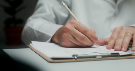 A male doctor writes in a notebook, making an appointment for treatment to a patient. Close-up of his hands, an unrecognizable person