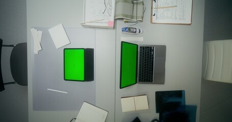 A laptop and a tablet with green screens are on the desktop of a doctor and a nurse at the clinic. View from above