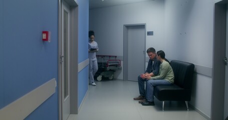 Relatives are waiting for the operation result, sitting in the hospital corridor and holding hands,...