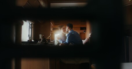 A man and a woman smile and kiss sitting on a bed in a van. Romantic trip