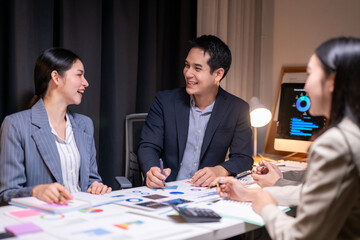A group of people are sitting around a table with papers and a computer monitor